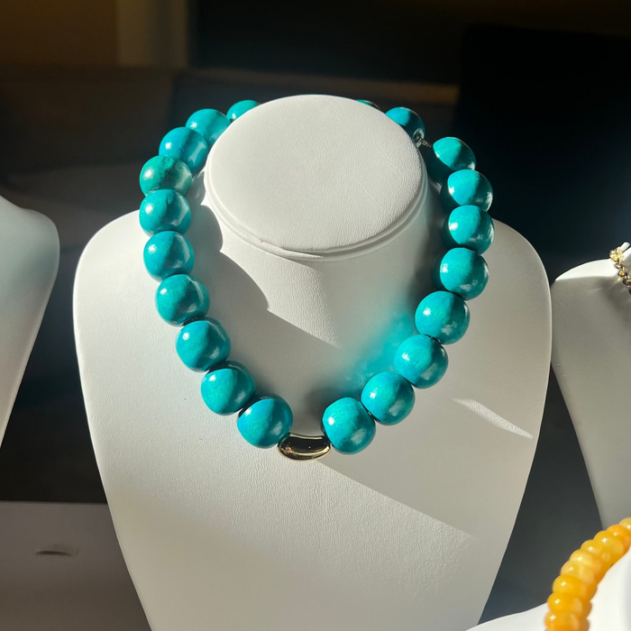 Turquoise beaded necklace on a white mannequin bust with other jewelry in the background.