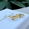 Gold hoop earrings with clear stones on a branded box with green leaves in the background