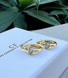 Gold hoop earrings with clear stones on a branded box with green leaves in the background