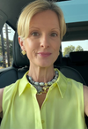 Woman in a car wearing a yellow sleeveless top and colorful necklace.