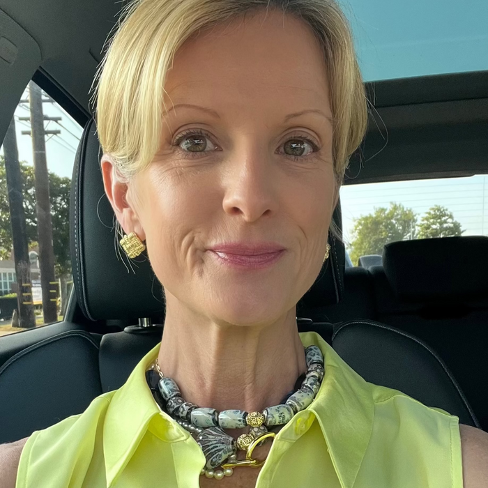 Woman in a car wearing a yellow sleeveless top and colorful necklace.