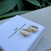 Gold hoop earrings on a white box with 'CF' branding, against a green leafy background.
