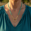 Gold necklace with a green cord worn by a person in a teal top.