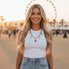 Woman in a white tank top and denim skirt standing in front of a Ferris wheel.