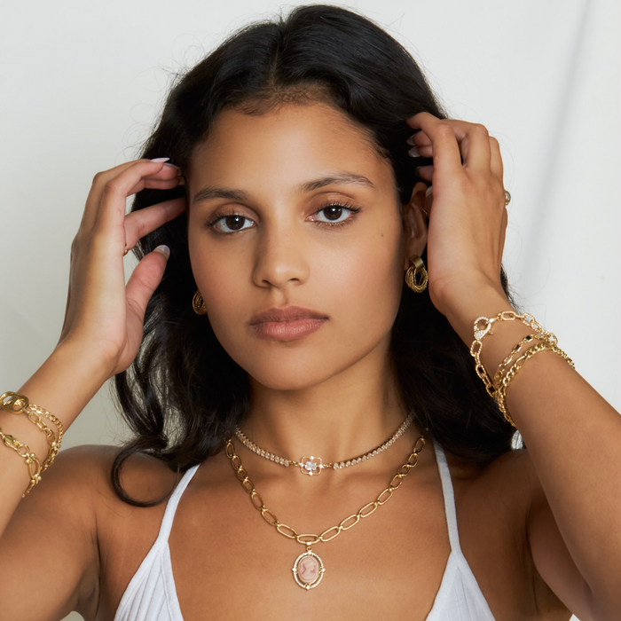 Woman wearing gold jewelry including necklaces, bracelets, and earrings against a white background