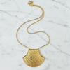 Gold necklace with a textured pendant on a marble surface