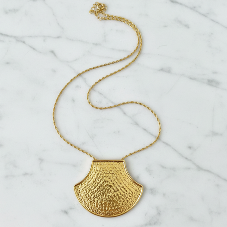 Gold necklace with a textured pendant on a marble surface