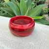 Red glass bracelet on a stone surface with green foliage in the background