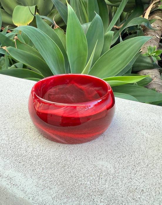 Red glass bracelet on a stone surface with green foliage in the background