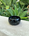 Black ceramic bracelet on a textured surface with green plants in the background
