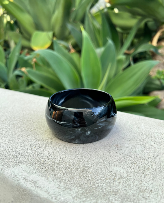 Black ceramic bracelet on a textured surface with green plants in the background