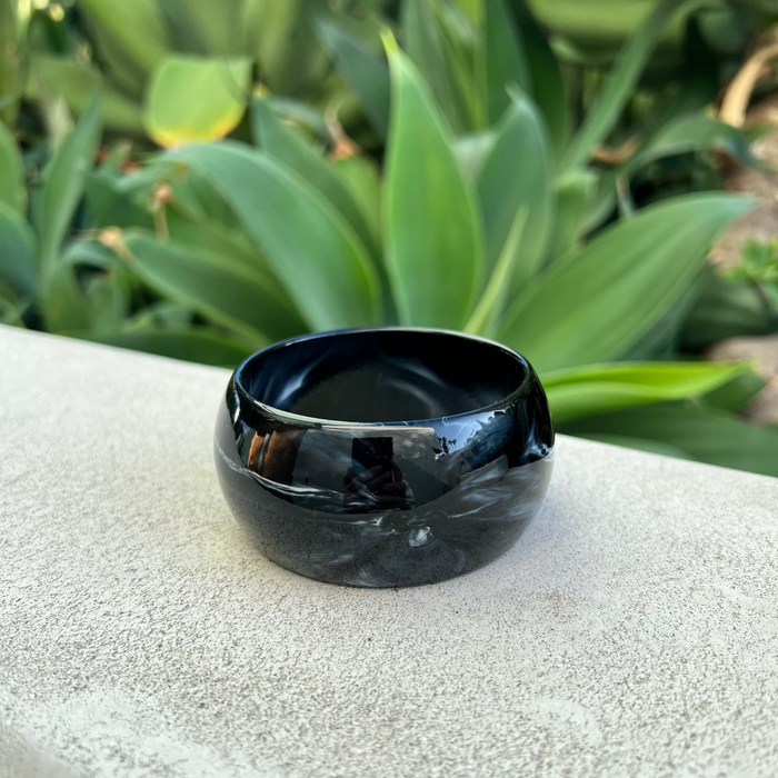 Black ceramic bracelet on a textured surface with green plants in the background