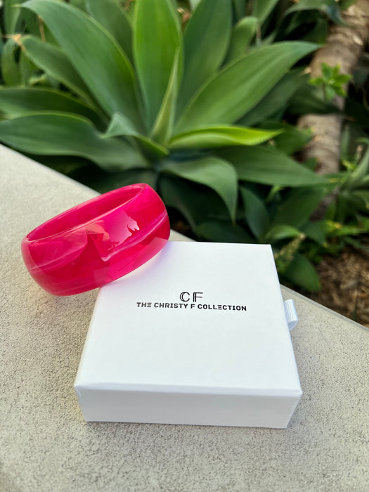 Pink bracelet on a white box with 'CF The Christy F Collection' branding, set against a green plant background.