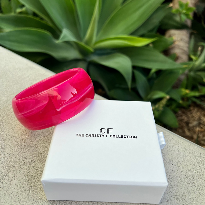 Pink bracelet on a white box with 'CF The Christy F Collection' branding, set against a green plant background.
