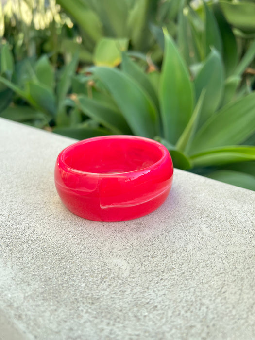 Pink bracelet on a textured surface with green foliage in the background