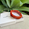 Red bracelet in a white box with 'The Christy F. Collection' branding, set against a green leafy background.