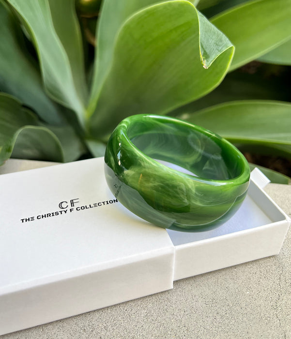 Green bracelet on a white box with 'CF' branding, set against a green leafy background.