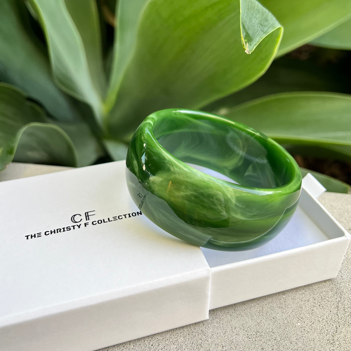 Green bracelet on a white box with 'CF' branding, set against a green leafy background.