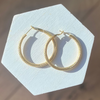 Gold hoop earrings on a white hexagonal stand with a neutral background