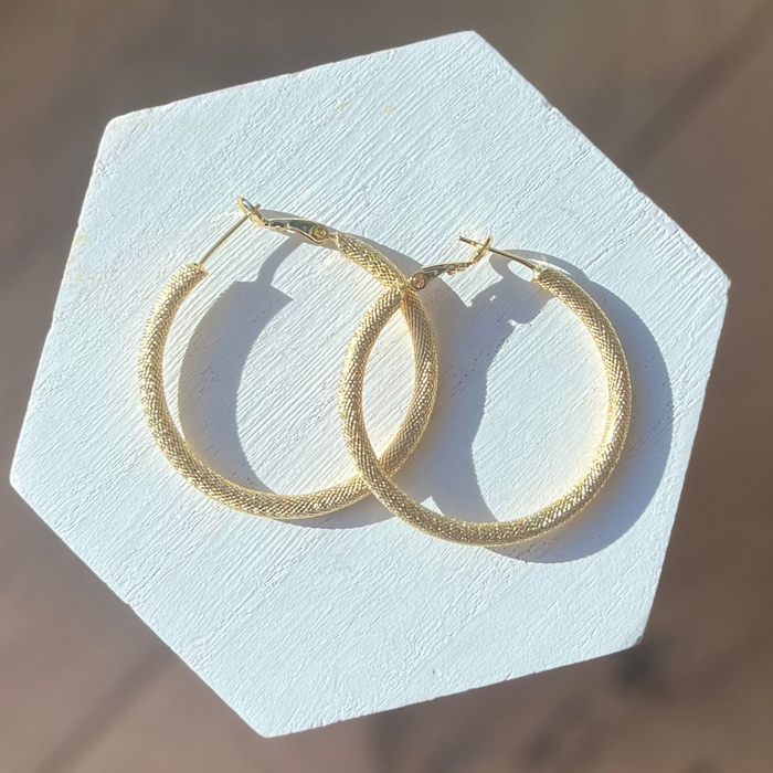 Gold hoop earrings on a white hexagonal stand with a neutral background