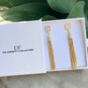 Gold tassel earrings in a box with 'The Christy F Collection' branding.