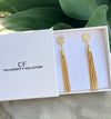 Gold tassel earrings in a box with 'The Christy F Collection' branding.