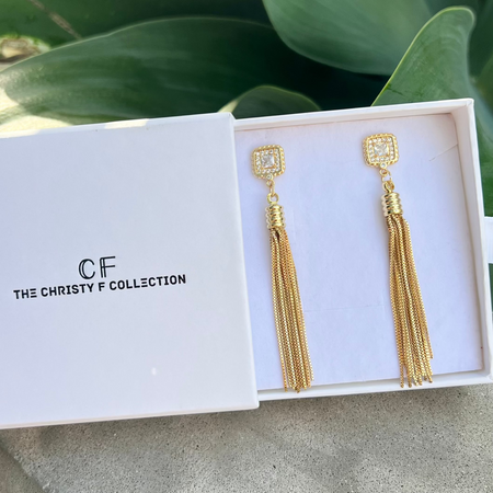 Gold tassel earrings in a box with 'The Christy F Collection' branding.