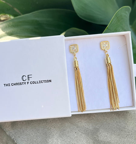 Gold tassel earrings in a box with 'The Christy F Collection' branding.