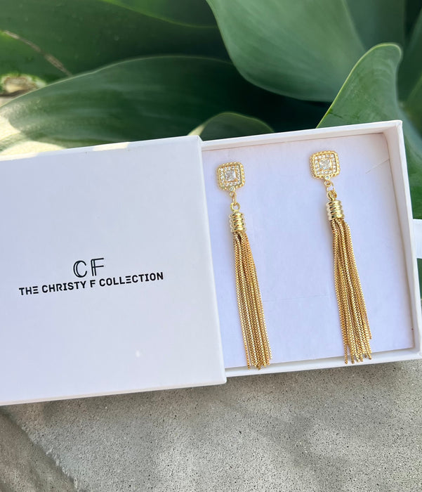 Gold tassel earrings in a box with 'The Christy F Collection' branding.