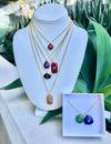 Set of necklaces with colorful pendants on a mannequin bust with a green plant background.