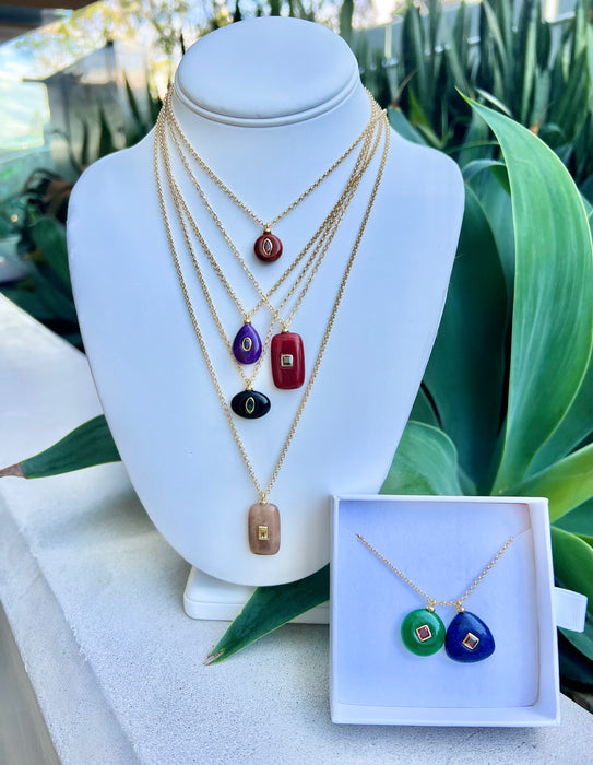 Set of necklaces with colorful pendants on a mannequin bust with a green plant background.