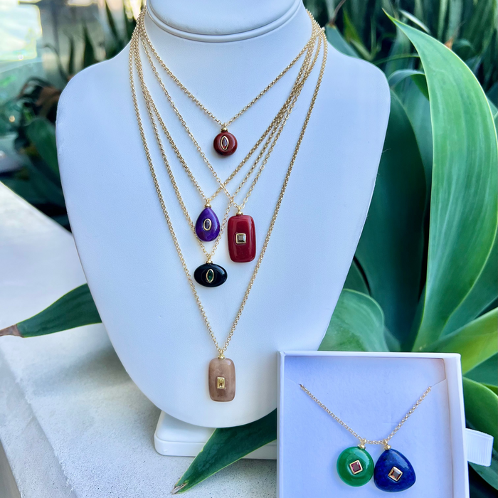 Set of necklaces with colorful pendants on a mannequin bust with a green plant background.