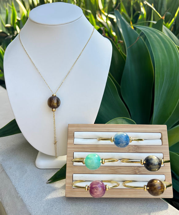 Necklace on a mannequin bust with a wooden display of rings featuring gemstones.