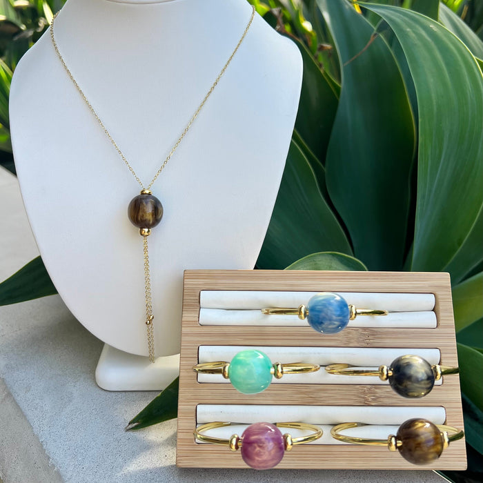Necklace on a mannequin bust with a wooden display of rings featuring gemstones.