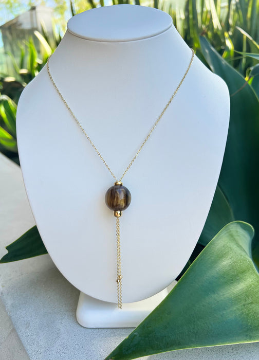 Necklace with a brown pendant on a white mannequin bust against a green leafy background