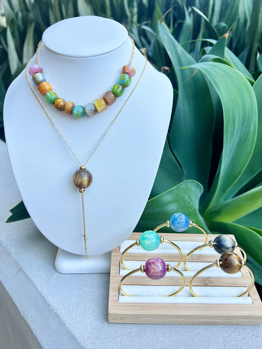Jewelry set with necklace and bracelet on a white stand with green plants in the background