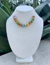 Colorful beaded necklace on a white mannequin bust with green plants in the background