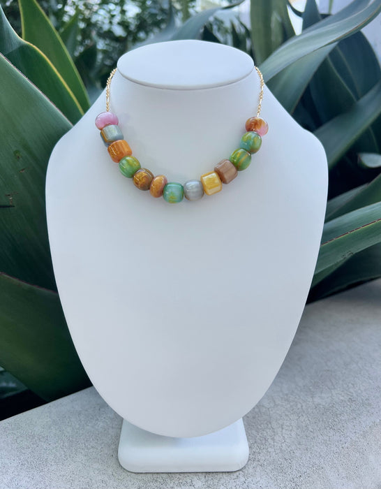 Colorful beaded necklace on a white mannequin bust with green plants in the background
