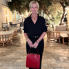 Woman in a black outfit holding a red handbag in an outdoor setting with tables and chairs.