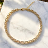 A gold-toned double-strand tennis-style necklace with clear rhinestones, displayed on a white marble surface.