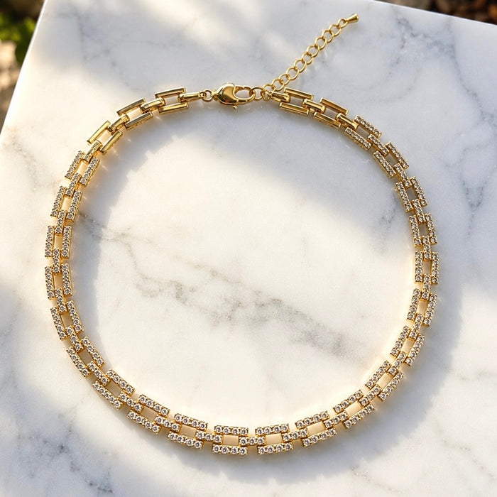 A gold-toned double-strand tennis-style necklace with clear rhinestones, displayed on a white marble surface.