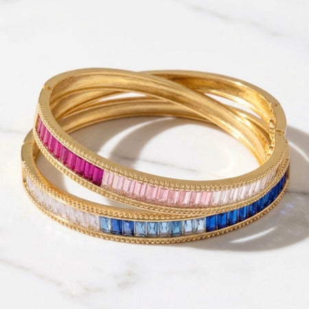 two ombre bangles one in blue and one in pink both with cubic zirconia baguettes on a marble background.