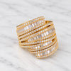 A wide gold wrap cuff ring paved with baguette-cut clear stones, displayed on a white marble surface.