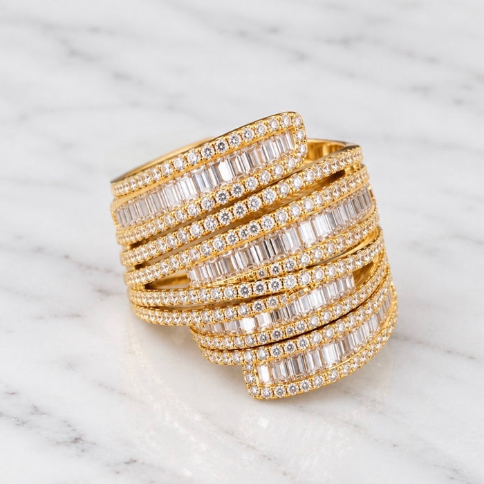 A wide gold wrap cuff ring paved with baguette-cut clear stones, displayed on a white marble surface.