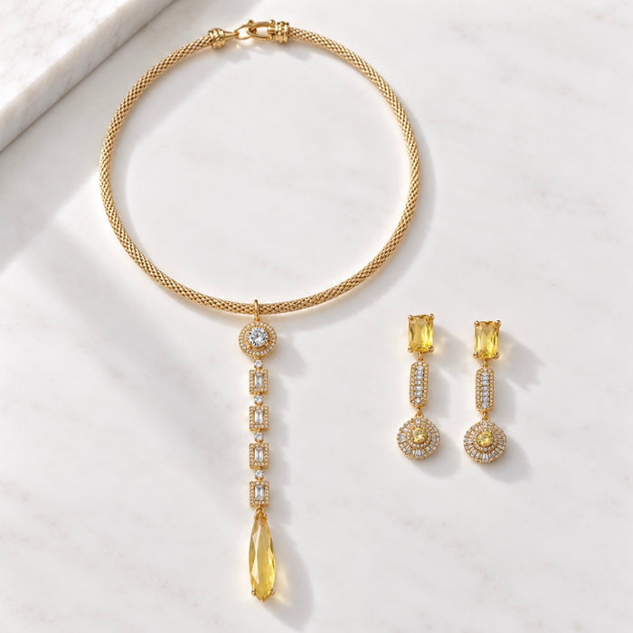 Gold jewelry set featuring a necklace and matching drop earrings with yellow gemstones and pavé accents, arranged on a light marble surface.