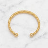A gold cable-wrapped cuff bracelet with polished ball-end closures, displayed on a white marble surface.