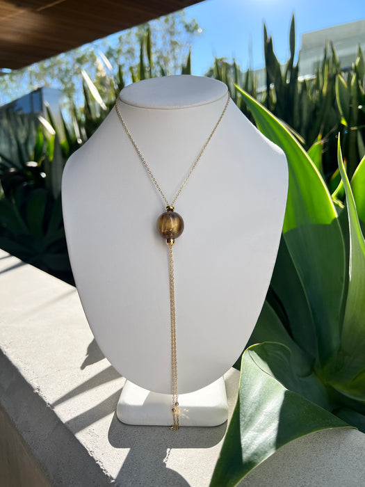 Gold necklace on a white mannequin bust with green foliage in the background