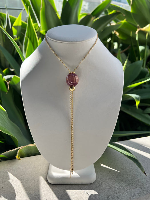 Necklace with a purple gemstone on a mannequin bust against a green leafy background
