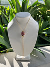 Necklace with a purple pendant on a mannequin bust against a green leafy background