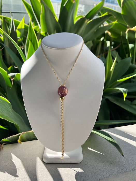 Necklace with a purple pendant on a mannequin bust against a green leafy background